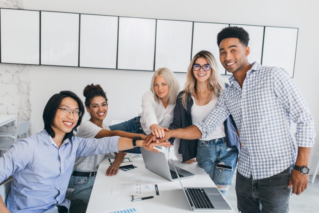 Portrait of asian young man and his african friend posing beside table with laptops and documents on it. Web-designer shaking hands with new employee in office.